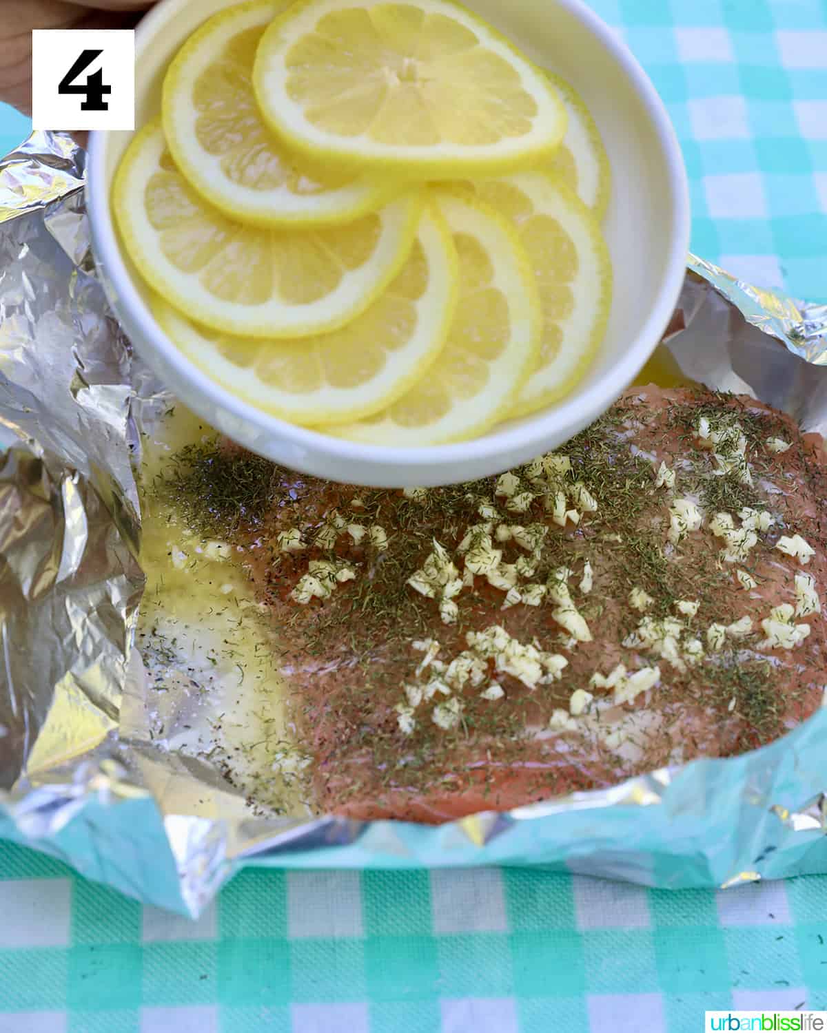bowl of lemon slices above garlic buttered salmon in foil on a checkered tablecloth.