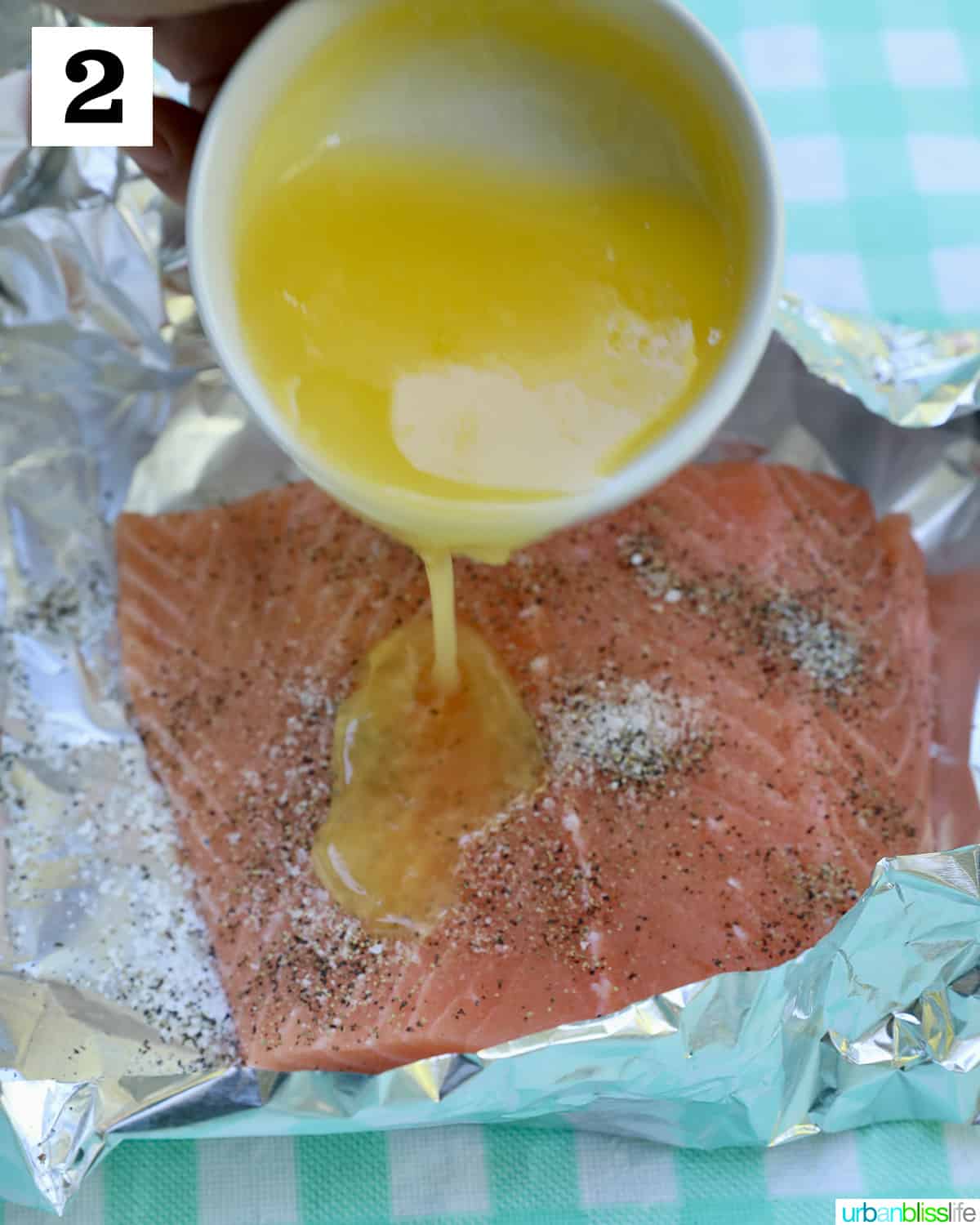 butter poured from a white bowl over seasoned salmon in foil.