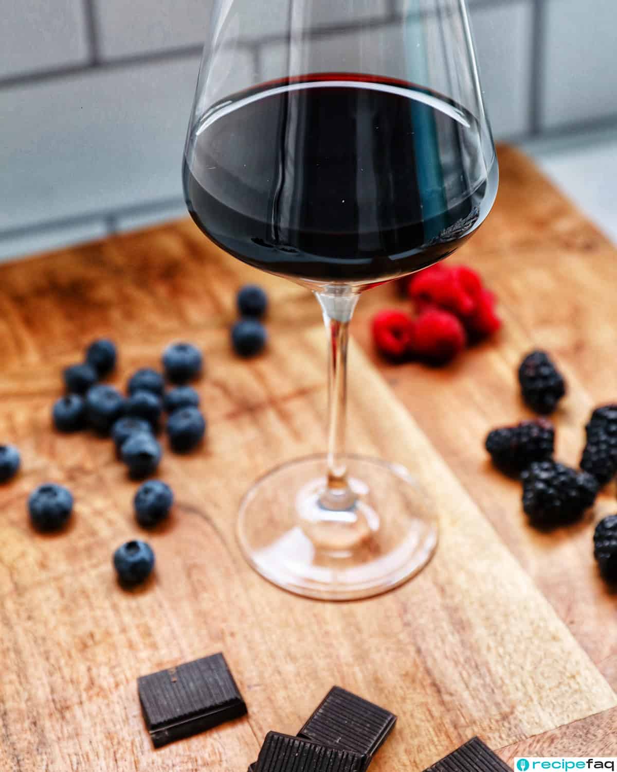 glass of zinfandel red wine on a wooden board with fresh fruits and chocolates around it.