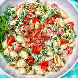 BLT pasta salad in a white bowl on an aqua checkered tablecloth.