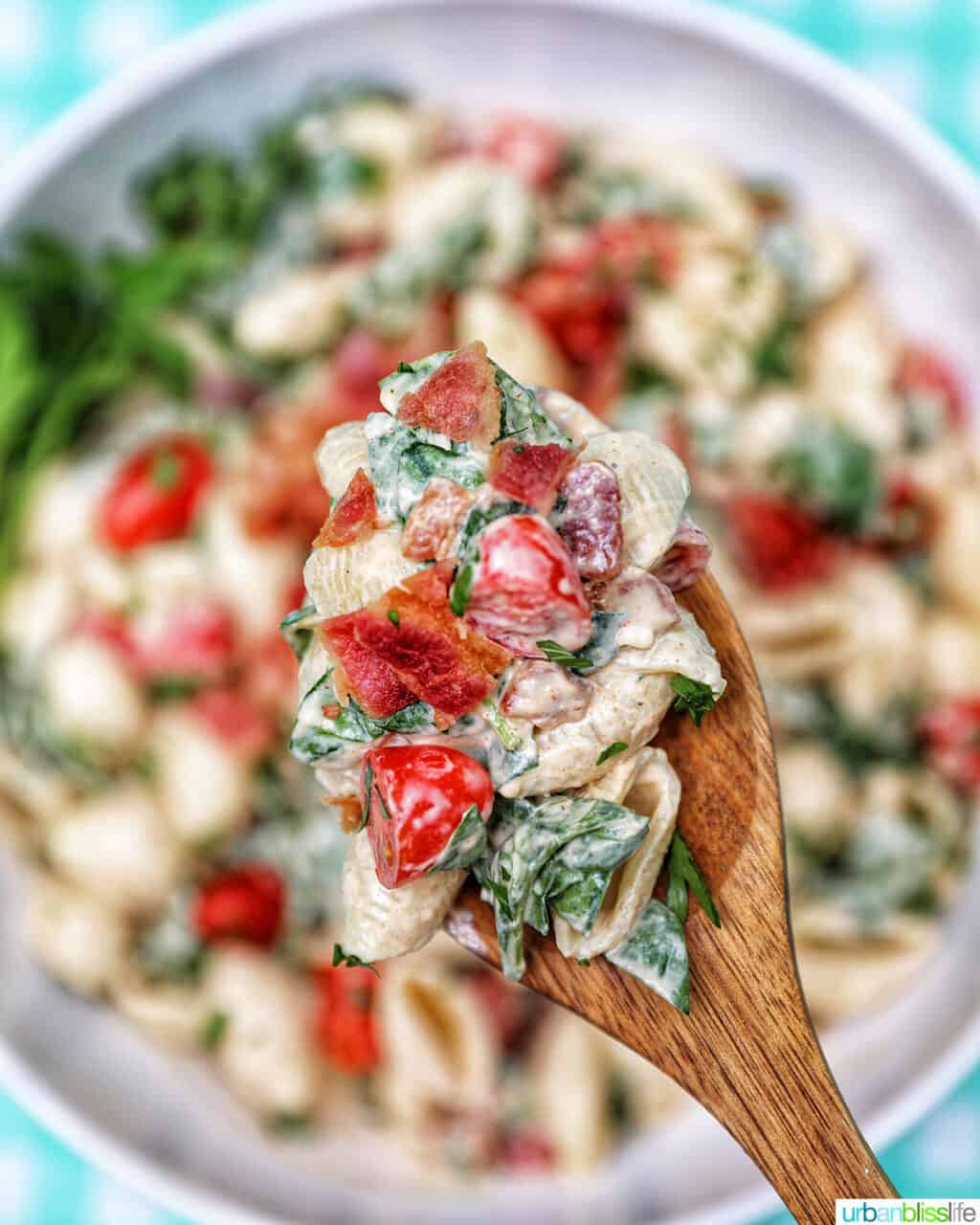 wooden serving spoon holding up a scoop of BLT pasta salad with pasta salad below blurred out.