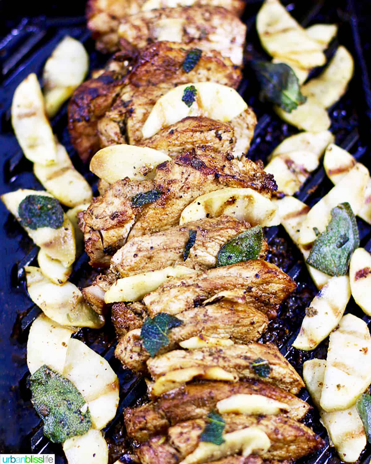 sliced grilled pork tenderloin on a grill pan with sliced apples and sage leaves.