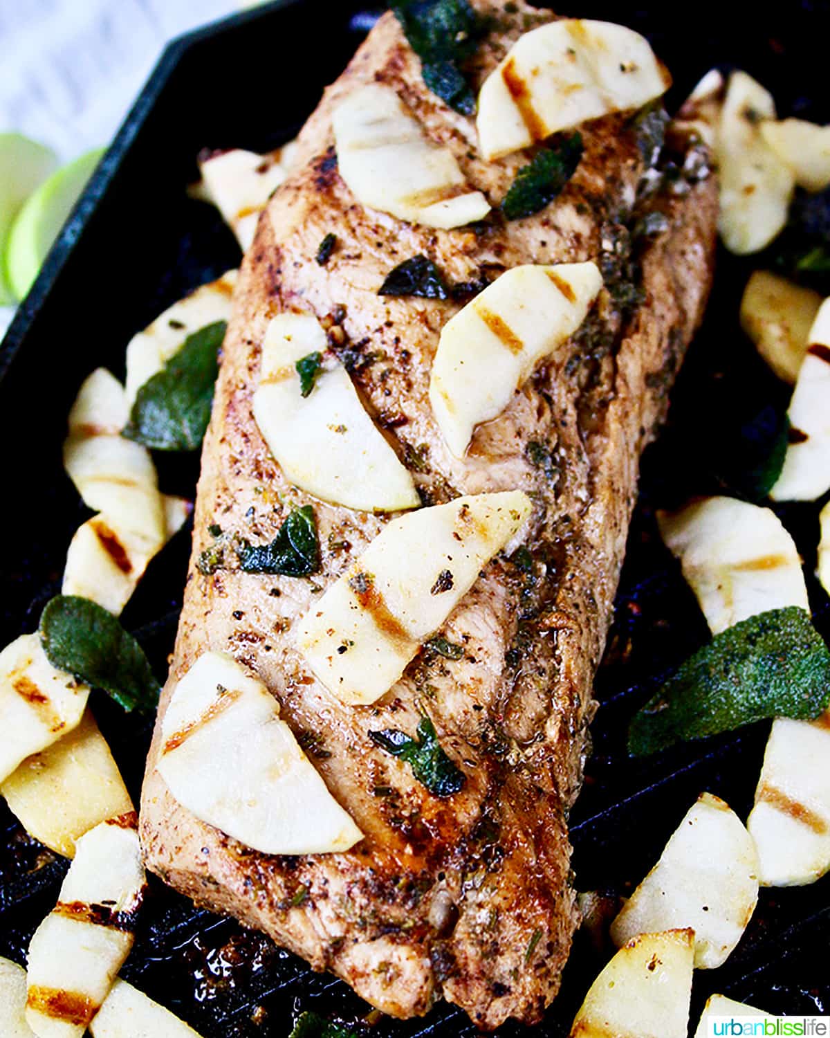 grilled pork tenderloin with apple slices and charred sage on a grill pan.