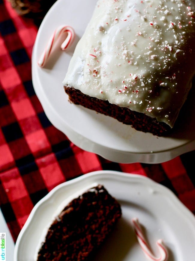 Gingerbread Loaf with Peppermint Cream Cheese Frosting sliced on a plate with candy canes and plaid tablecloth.