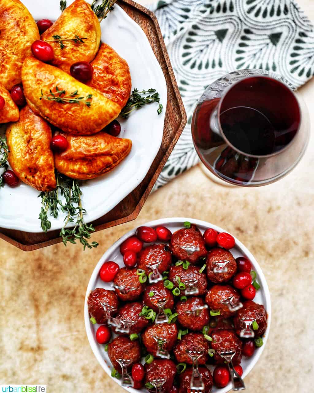 holiday appetizers of cranberry meatballs, mushroom empanadas, and glass of red wine
