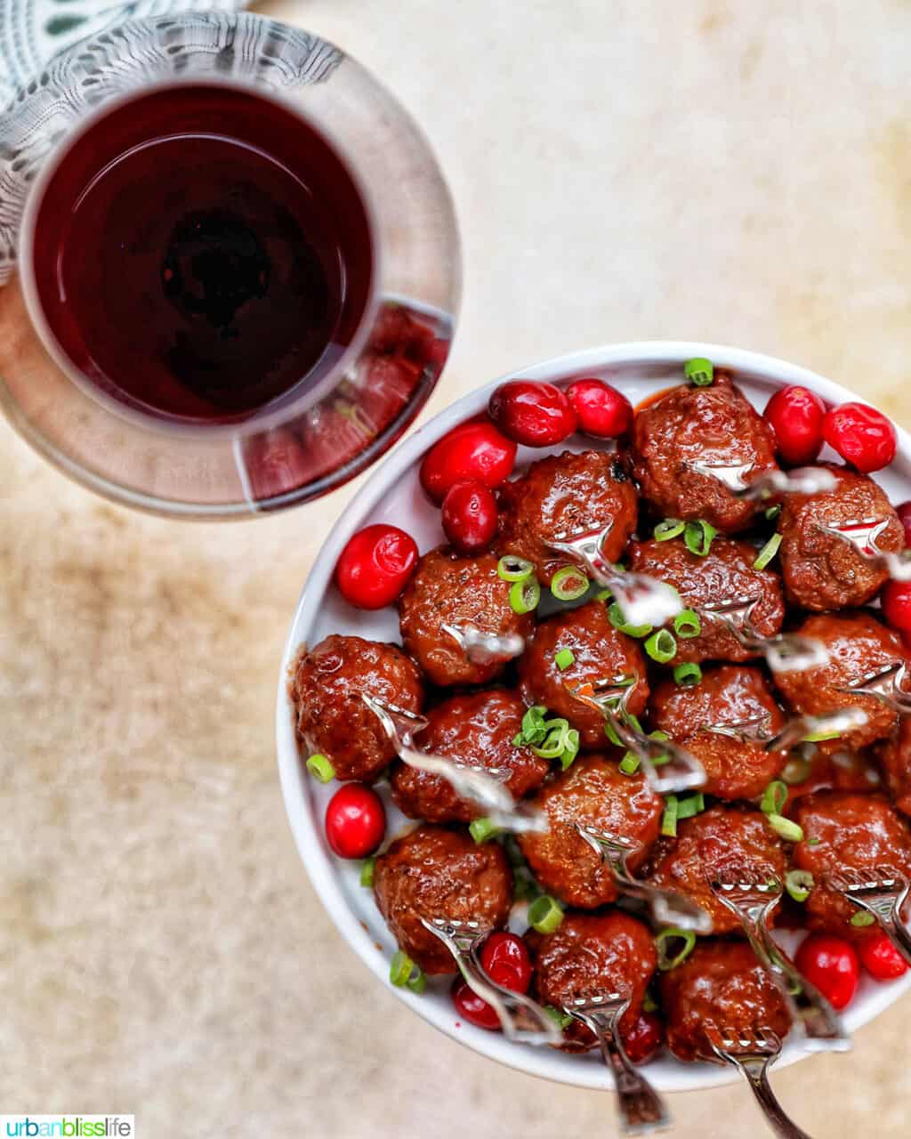 red wine glass next to plate of cranberry meatballs
