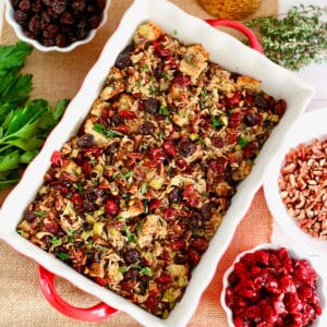 cranberry stuffing with wild rice and cherries in a casserole dish with bowls of cherries and herbs on the side.