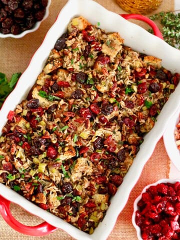 cranberry stuffing with wild rice and cherries in a casserole dish with bowls of cherries and herbs on the side.