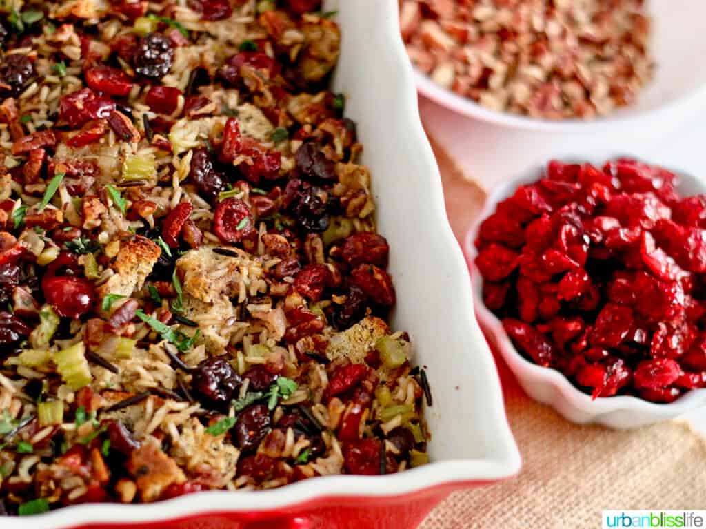 cranberry stuffing with wild rice and cherries in a casserole dish with bowls of cherries and herbs on the side.