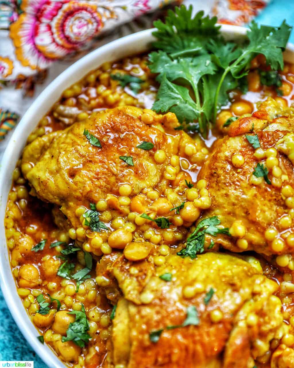 close up of left side of pressure cooker moroccan chicken in a large serving bowl with colorful napkin