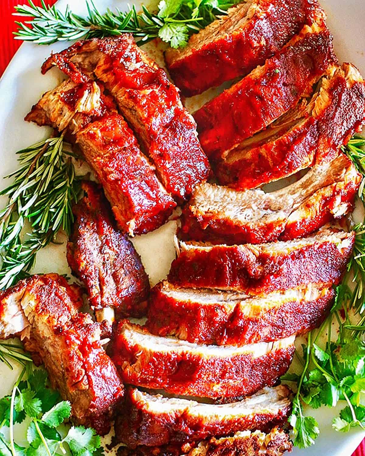 plate full of sliced instant pot pork ribs with rosemary and other herbs.