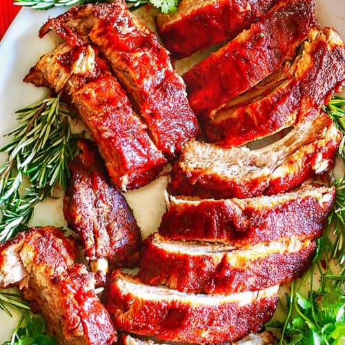 plate full of sliced instant pot pork ribs with rosemary and other herbs.