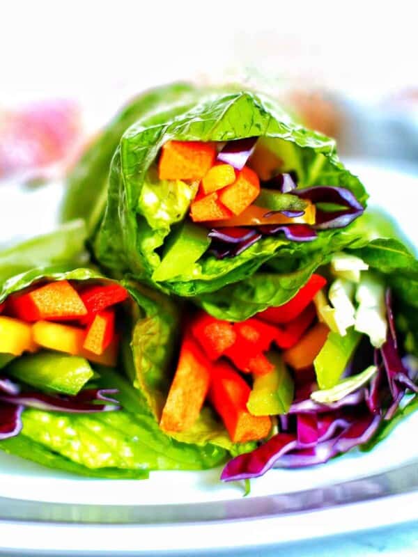 three rainbow salad rolls stacked on a plate.
