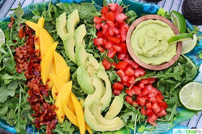 sliced avocados, mangos, tomatoes, and chopped bacon with avocado lime dressing