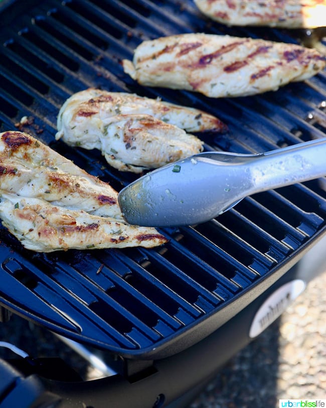 Grilled lemon pepper chicken on the grill with tongs.