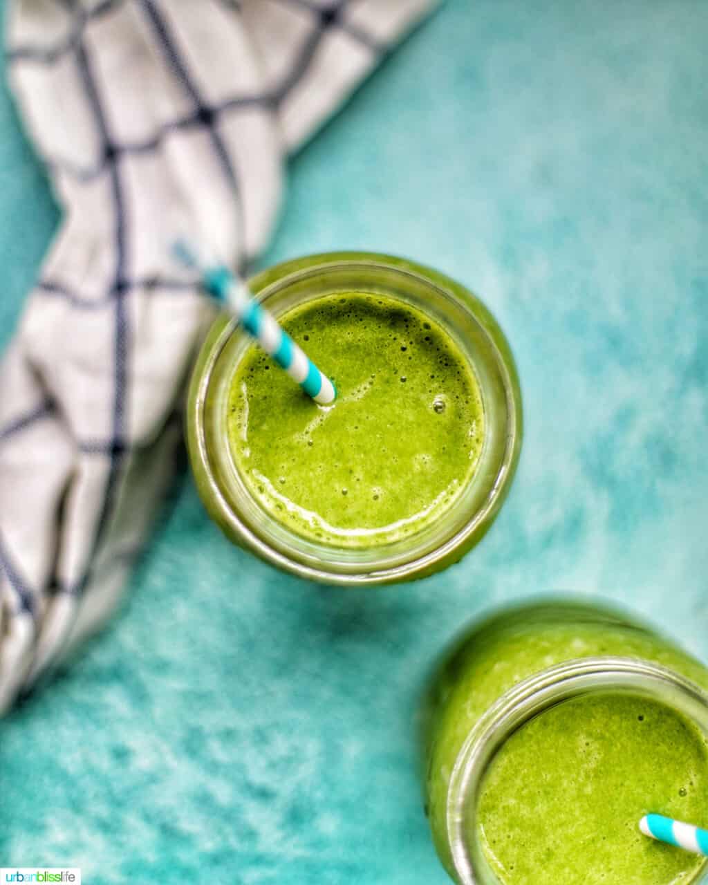 flatlay photo of two jars of green smoothies on blue background with a white tea towel