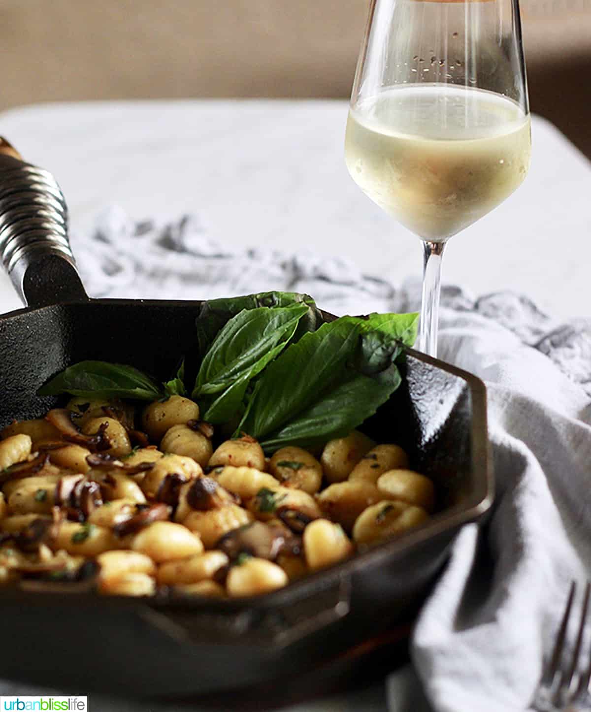 cast iron skillet with gnocchi, mushrooms, basil, glass of wine.