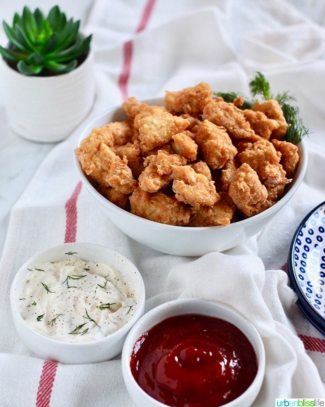bowl full of crispy Air Fryer Popcorn Chicken with dipping sauces and a small plant in the background.