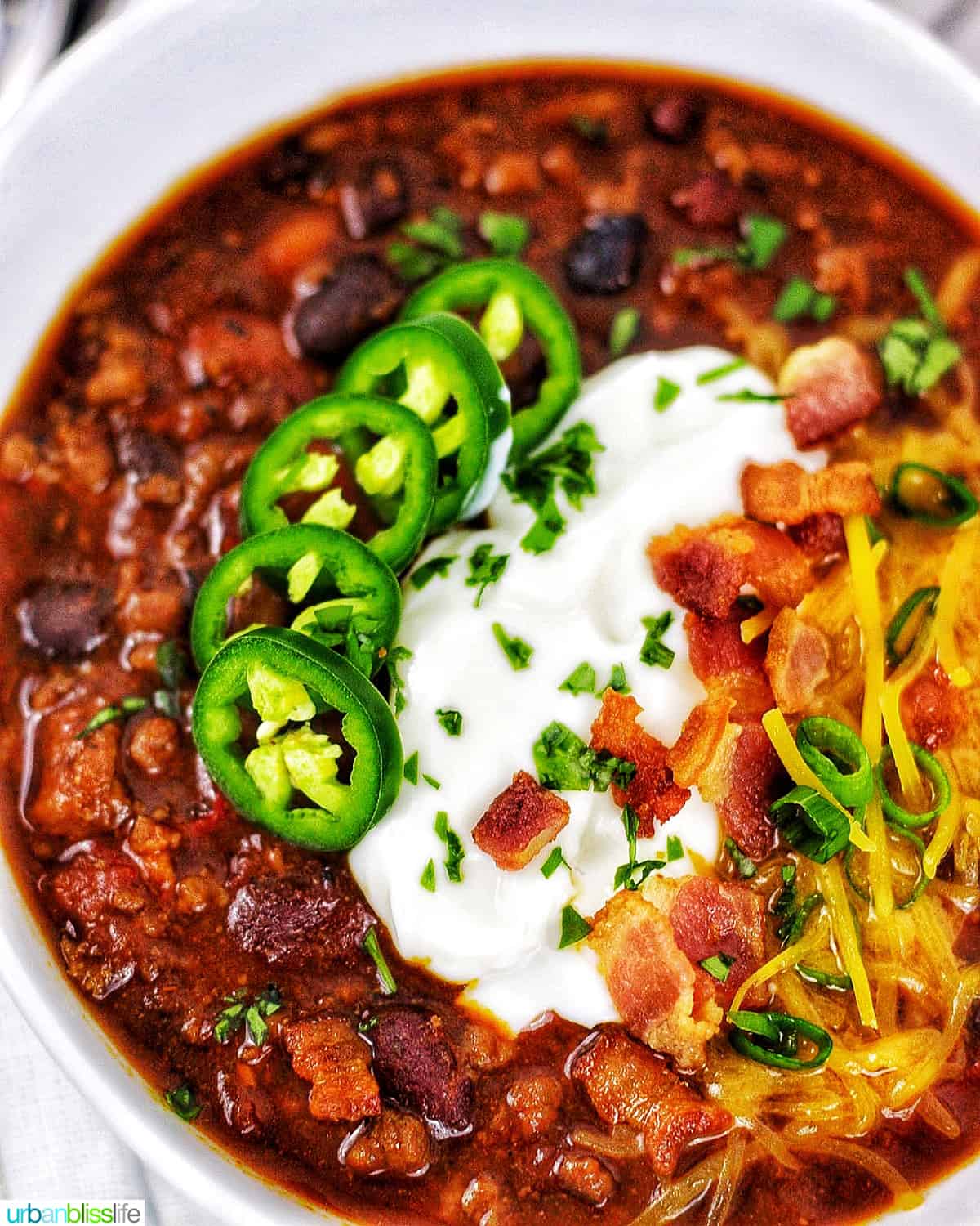 closeup of bowl of instant pot chili topped with jalapenos, sour cream, bacon, cheddar cheese,