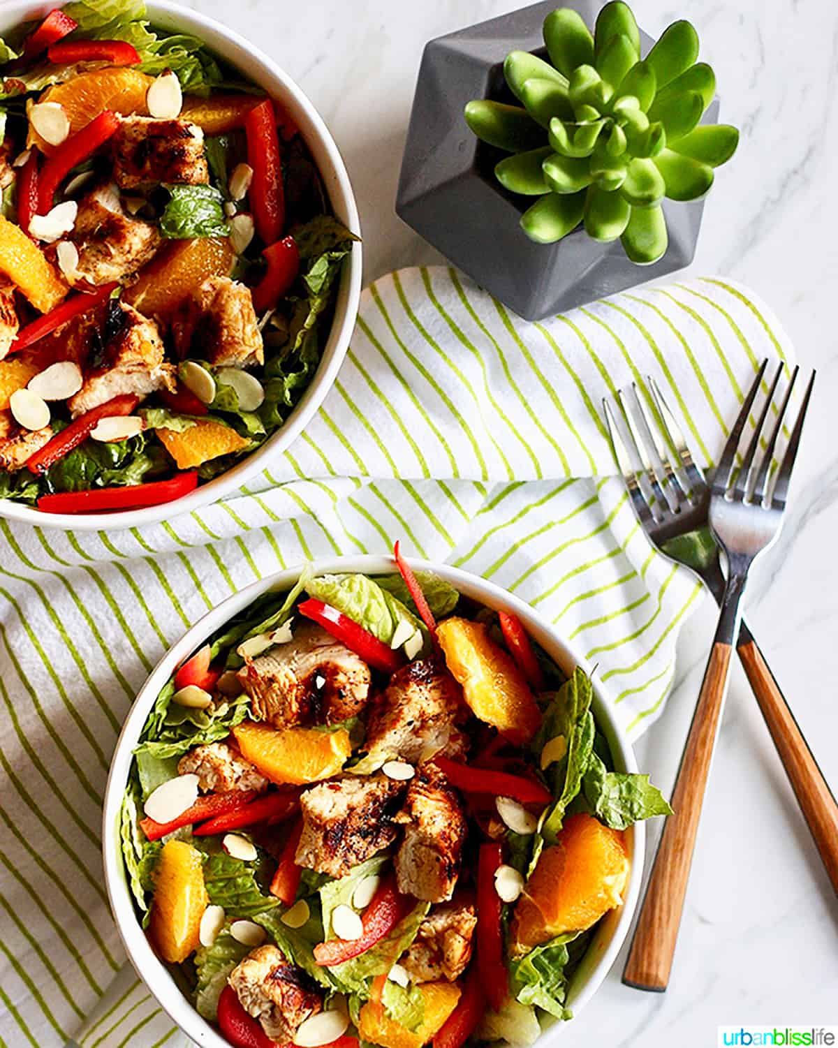 two bowls of mandarin orange chicken salad with two forks and a green and white napkin.