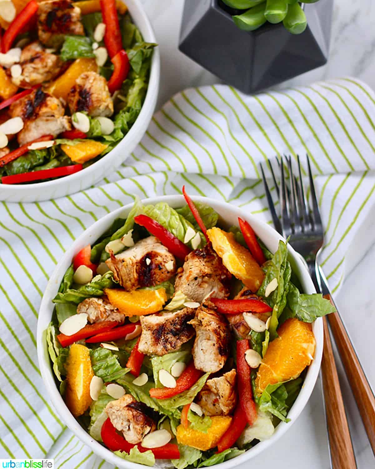 two bowls of mandarin orange chicken salad with two forks and a green and white napkin.