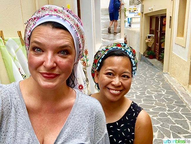 Amelia Old and Marlynn Schotland wearing traditional Greek scarves on a stone street in Olympos Village, Karpathos, Greece.