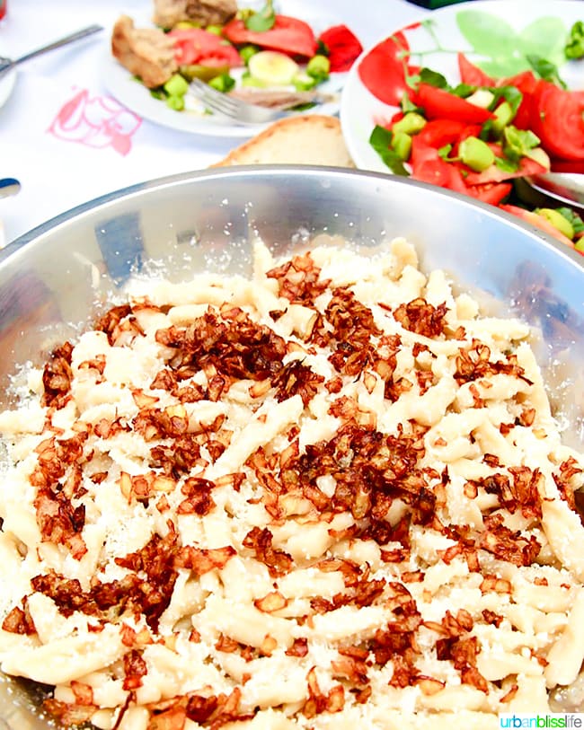 bowl full of traditional Makarounes filling pasta with tomato salad in background.