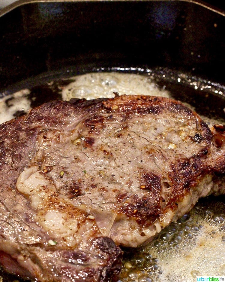 Cast iron rib eye steak cooking with butter.