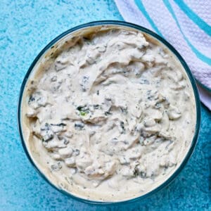 dairy free spinach dip in a bowl on a bright blue background with blue and white striped napkin.
