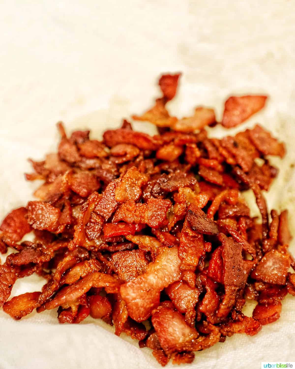 crispy cooked bacon draining fat on a paper towel lined plate.