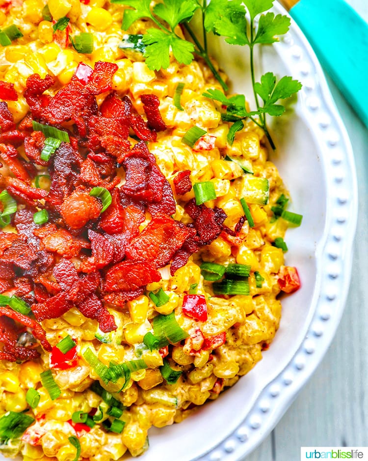 corn with bacon, green onions, red peppers and cream cheese in a large white serving bowl.