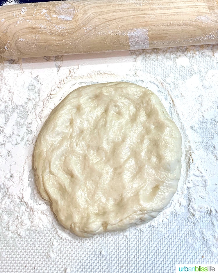 rolling pin above kneaded pizza dough on a floured surface, ready to roll out.