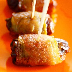 bacon-wrapped dates on toothpicks on an orange plate.