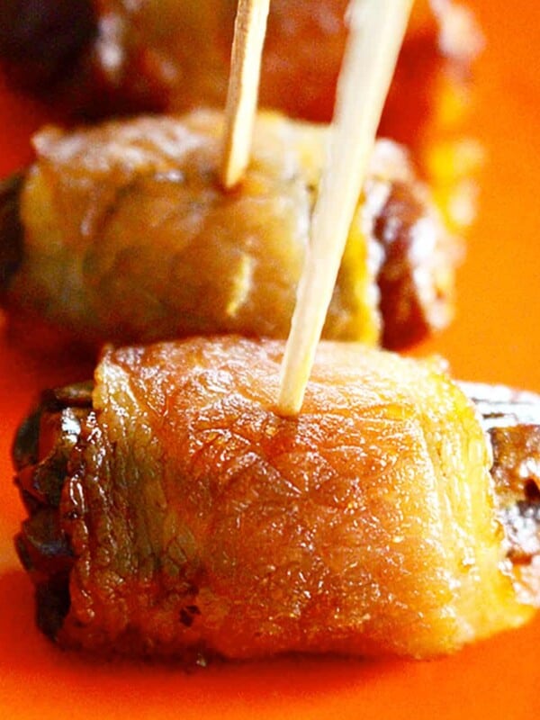 bacon-wrapped dates on toothpicks on an orange plate.