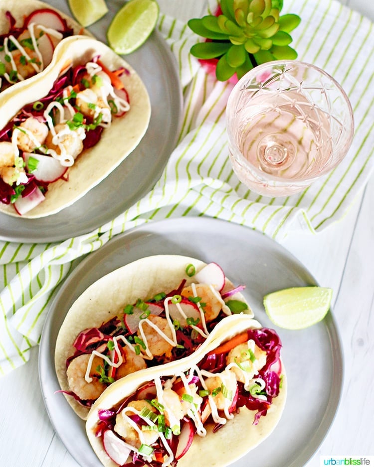 flatlay of two plates of shrimp tacos with a glass of rosé wine