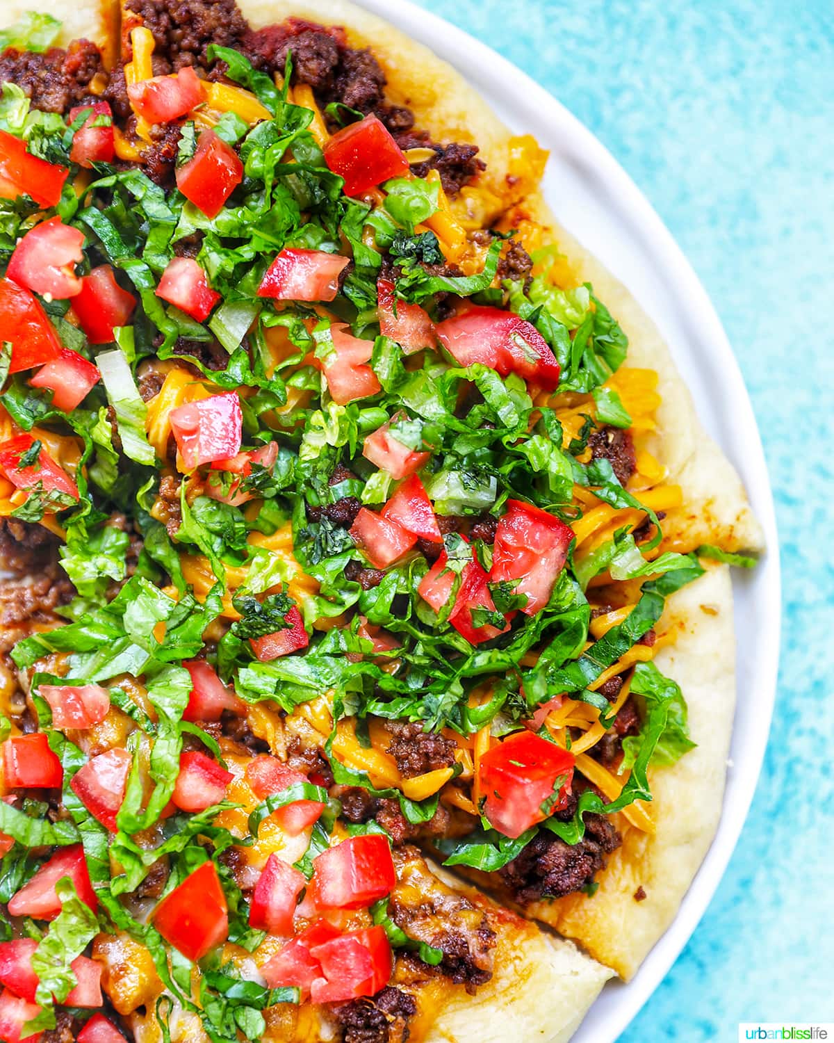 homemade taco pizza on a white plate and blue background.