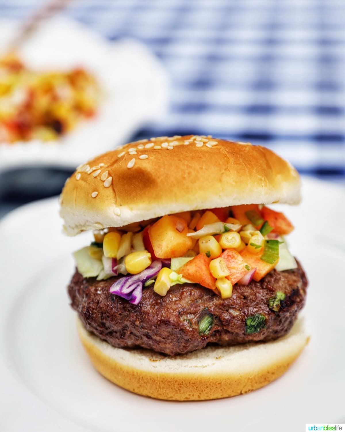 Asian beef burger with corn and cabbage slaw on a white plate.