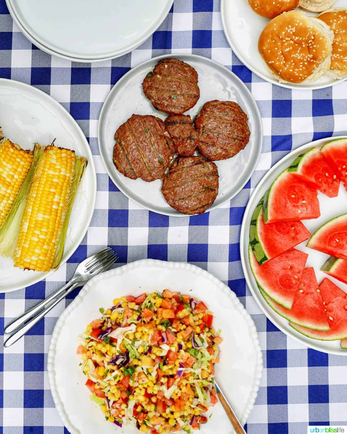 Asian burgers with slaw, corn on the cob, watermelon slices, and buns.