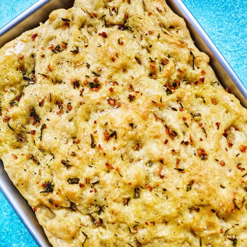 garlic rosemary focaccia bread in a baking sheet on bright blue background.