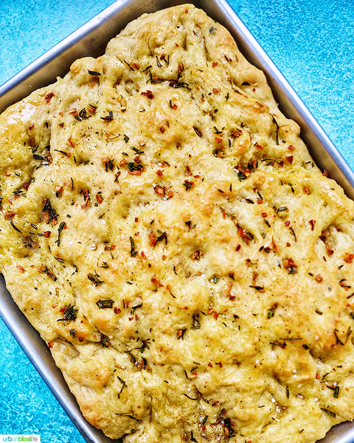 garlic rosemary focaccia bread in a baking sheet on bright blue background.