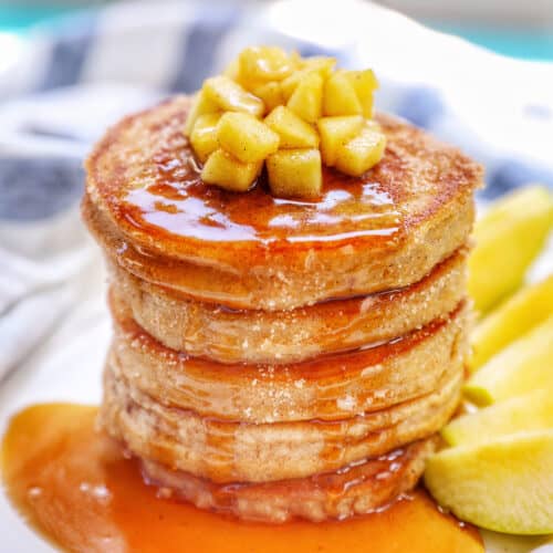 Stack of apple cinnamon pancakes topped with maple syrup and diced apples.
