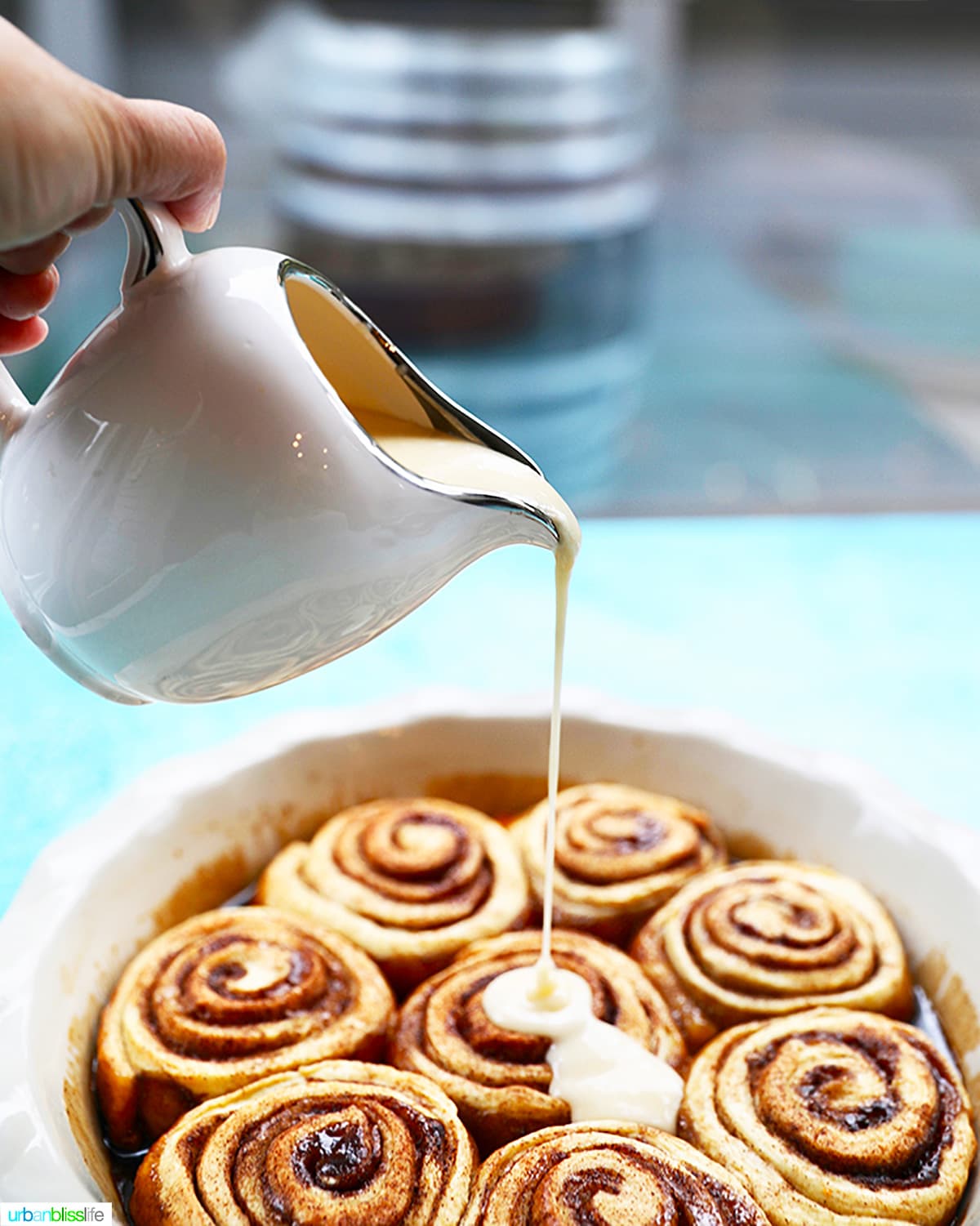 pouring icing over orange cinnamon rolls in a round baking dish.