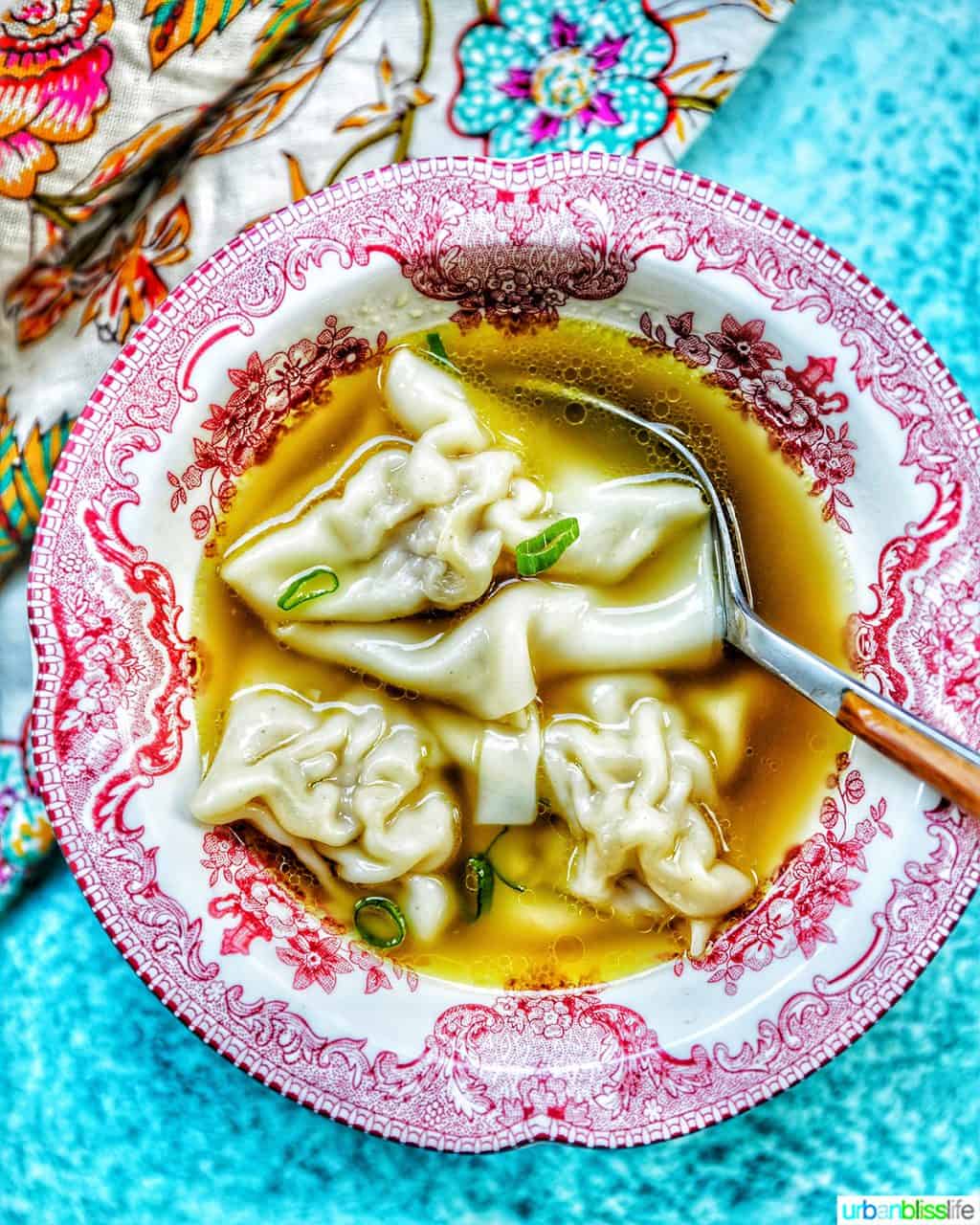 single bowl of wonton noodle soup with spoon, colorful napkin, and blue background