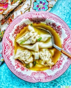 single bowl of wonton soup with spoon, colorful napkin, and blue background