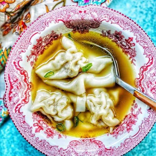 single bowl of wonton soup with spoon, colorful napkin, and blue background