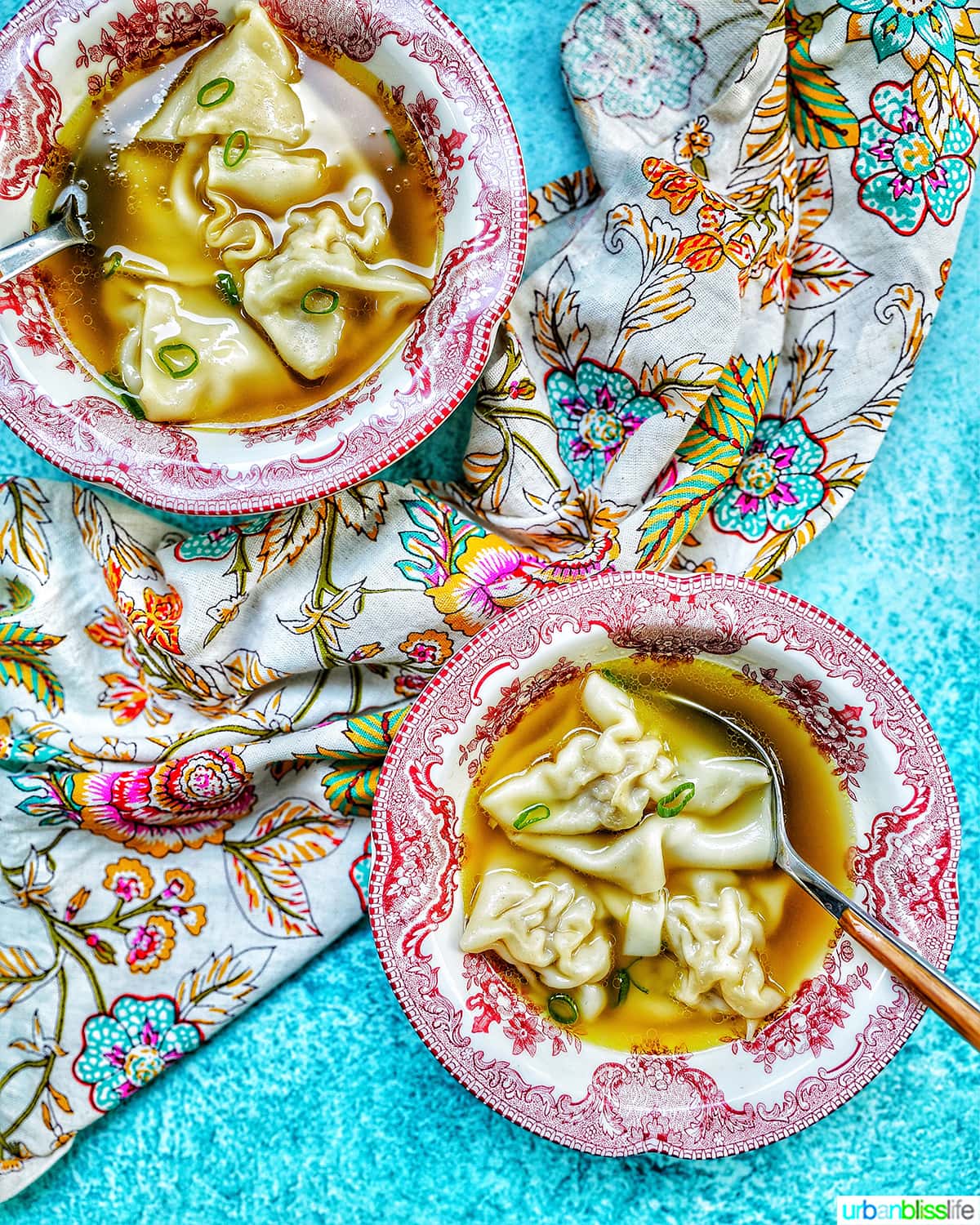 two bowls of wonton noodle soup with spoon, colorful napkin, and blue background