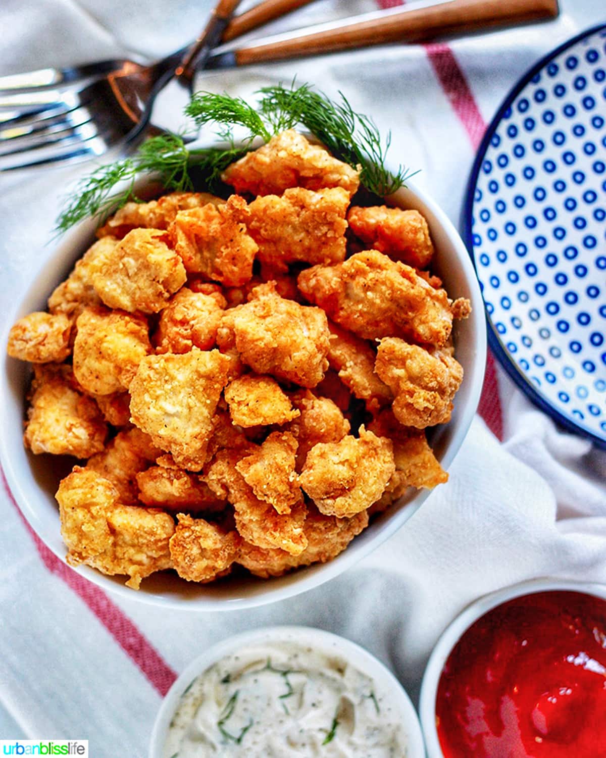 bowl full of crispy Air Fryer Popcorn Chicken with dipping sauces, a white and red striped napkin, forks and extra plates.