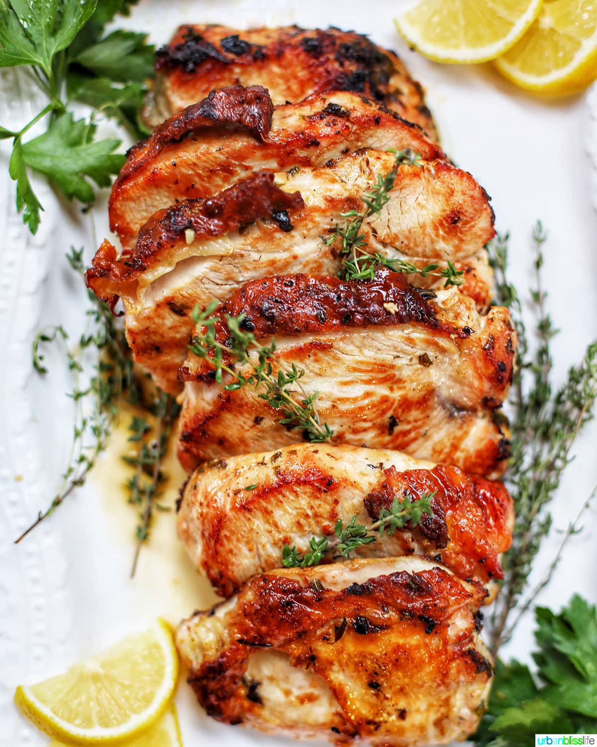 sliced Citrus Herb Turkey Breast with herbs and lemon slices on white platter.