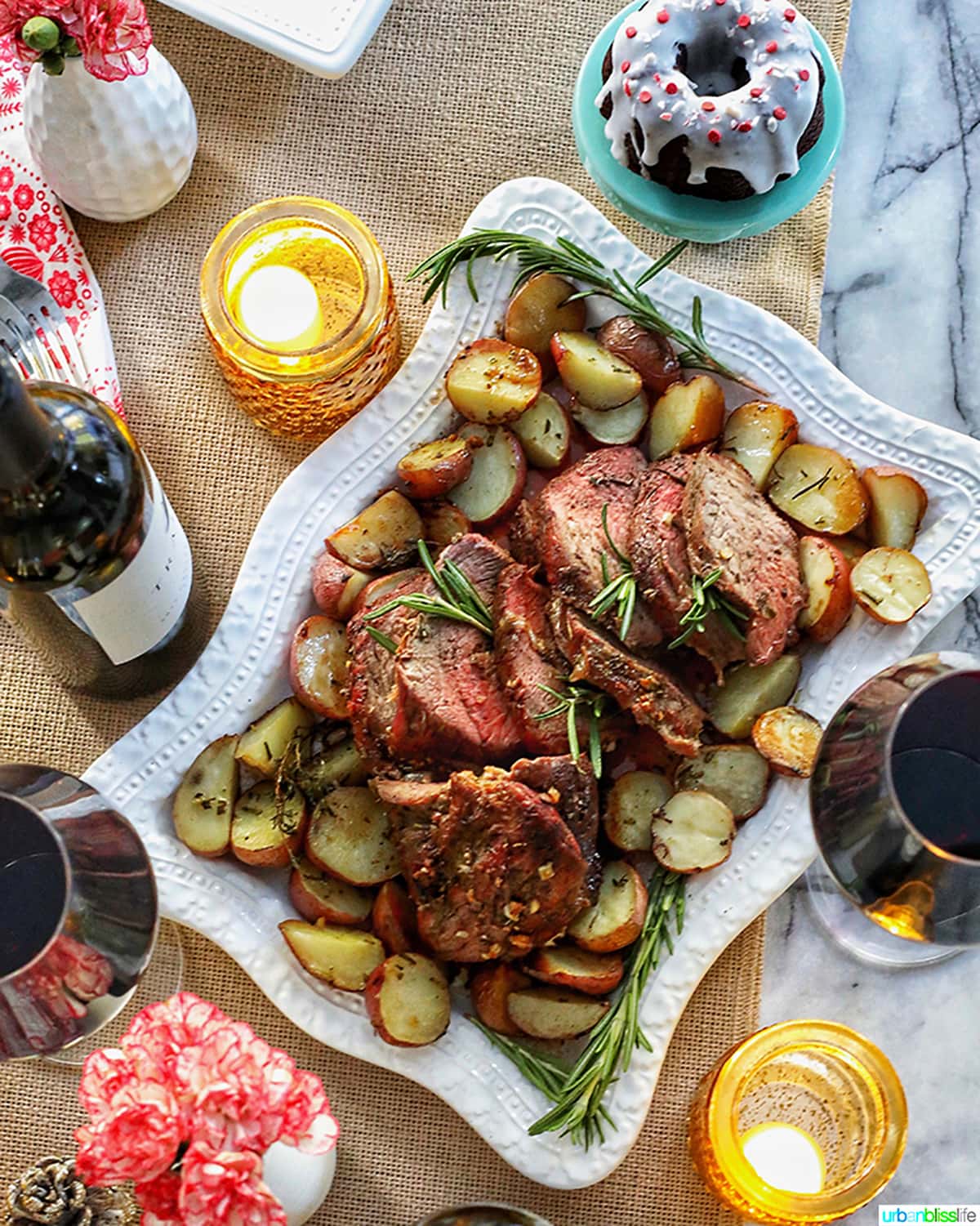 beef roast on white platter with wine glasses and candles