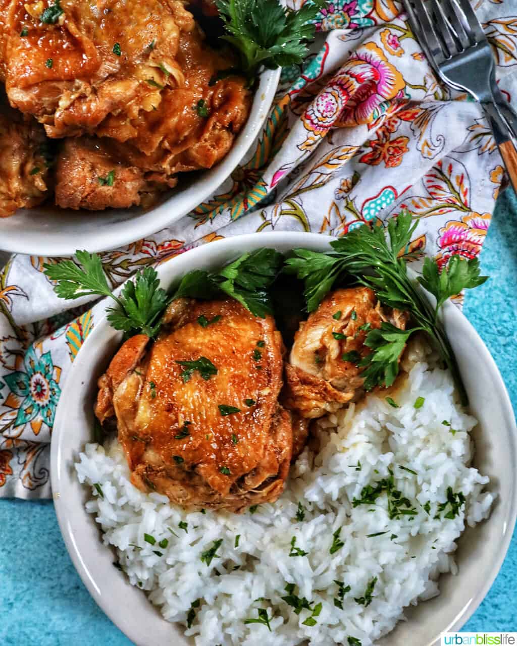 two bowls of Instant Pot Filipino Chicken Adobo and rice, with a colorful floral napkin and forks.